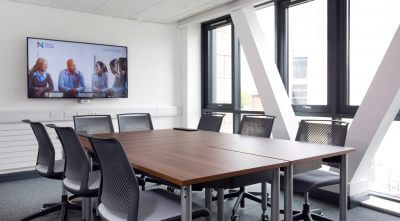 A meeting room with AV equipment on the wall. A table and chairs are in the middle of the room.